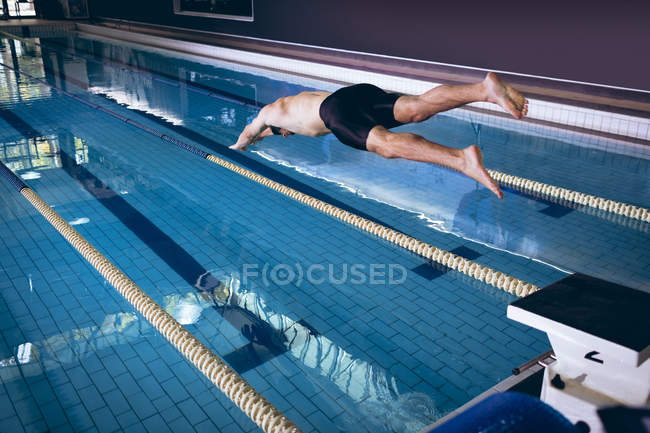 Vista posteriore di un nuotatore caucasico di sesso maschile con cuffia e occhiali bianchi che si tuffa in piscina — Foto stock