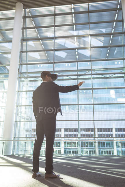Visão de baixo ângulo do empresário usando fones de ouvido de realidade virtual em um prédio de escritórios moderno — Fotografia de Stock