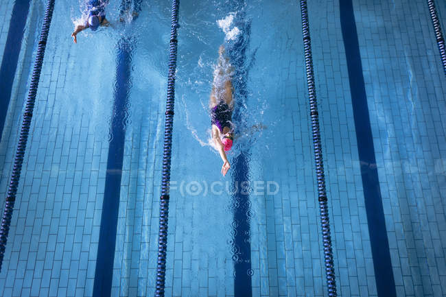 Vista de alto ângulo de uma mulher caucasiana vestindo um maiô e um boné de banho rosa fazendo freestyle acidente vascular cerebral na piscina — Fotografia de Stock