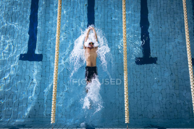 Vista ad alto angolo di un nuotatore caucasico maschio che indossa un berretto da nuoto bianco e occhiali che fanno un colpo alla schiena in piscina — Foto stock