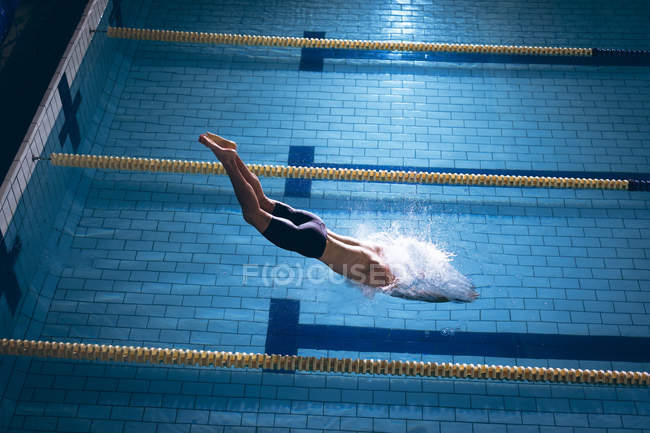 Vue grand angle d'un homme nageur caucasien portant un bonnet blanc plongeant dans la piscine — Photo de stock