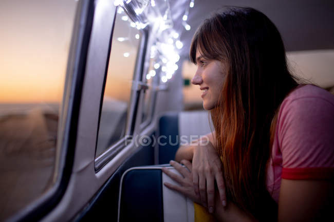 Vista lateral da mulher caucasiana feliz olhando através da janela de uma van campista na praia — Fotografia de Stock