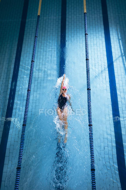 High angle view of a Caucasian woman wearing a pink swimming cap and goggles doing a back stroke in a swimming pool — Stock Photo