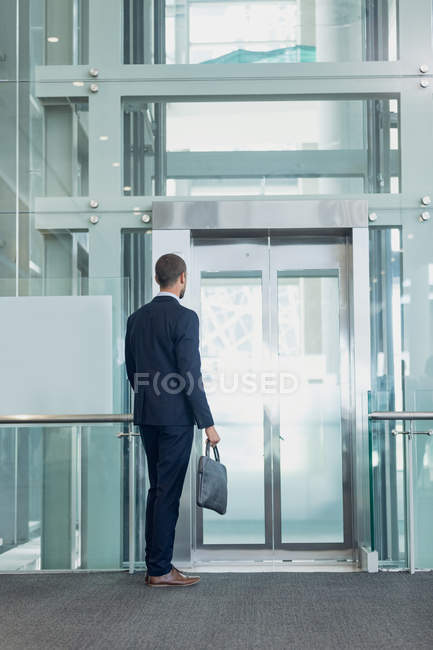 Visão traseira do executivo masculino caucasiano esperando o elevador no escritório moderno — Fotografia de Stock