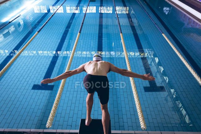 Vista posteriore di un nuotatore caucasico maschio che indossa un berretto bianco che si tuffa in piscina — Foto stock