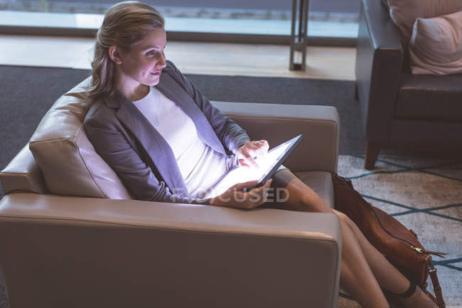 Вид сбоку красивой бизнесвумен, работающей на цифровом планшете на диване в фойе современного офиса — стоковое фото