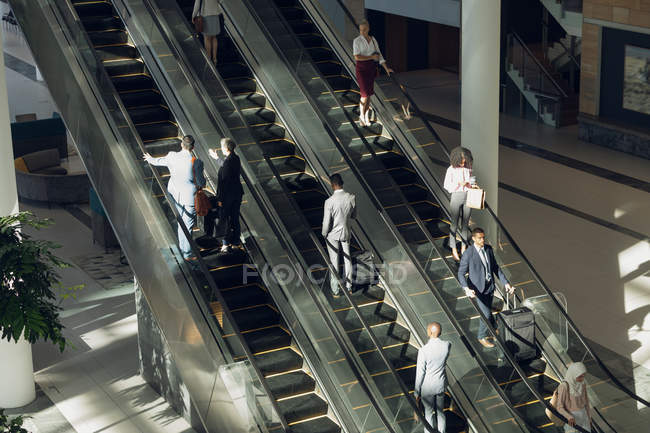 Vue aérienne de divers hommes d'affaires utilisant des escaliers roulants dans un bureau moderne — Photo de stock