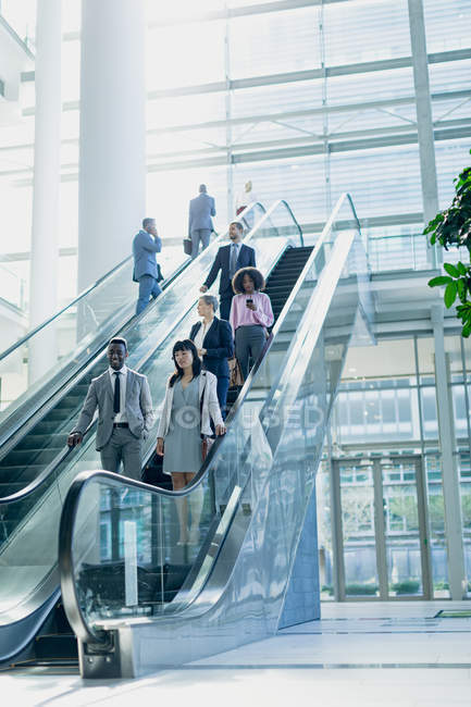 Vue latérale de divers hommes d'affaires utilisant des escaliers roulants dans un bureau moderne — Photo de stock