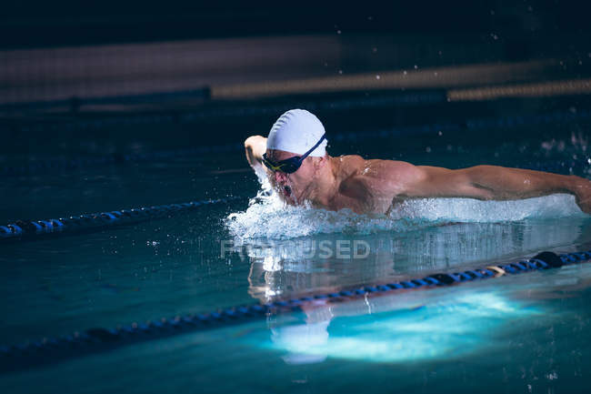Side view of a male Caucasian swimmer in the goggles and white swimming cap in the swimming pool — Stock Photo