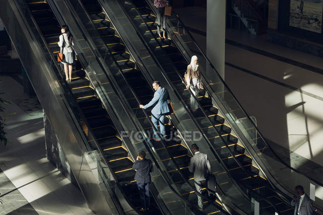 Vista aérea de diversos empresarios que utilizan escaleras mecánicas en oficinas modernas - foto de stock