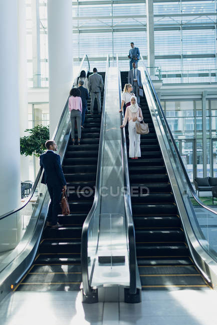 Vista frontale di diversi uomini d'affari che utilizzano scale mobili in un ufficio moderno — Foto stock