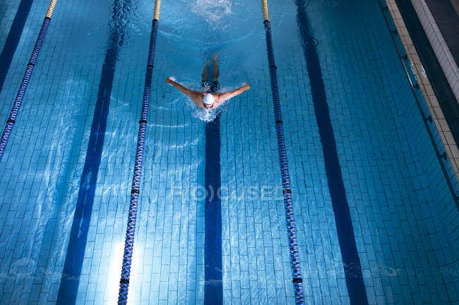 High angle view of a male Caucasian swimmer wearing a white swimming cap doing a butterfly stroke in the swimming pool — Stock Photo