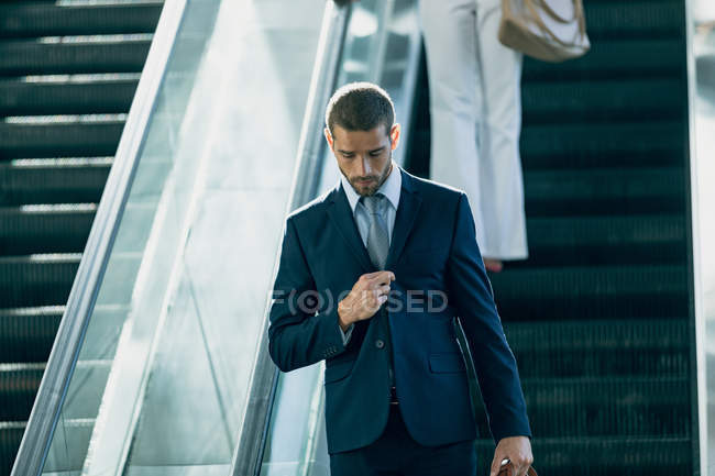 Vista frontal del hombre de negocios caucásico utilizando escaleras mecánicas en la oficina moderna - foto de stock