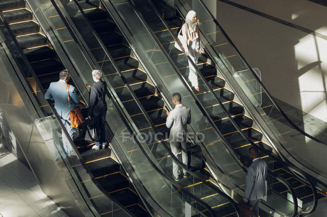 Vista aérea de diversos empresarios que utilizan escaleras mecánicas en oficinas modernas - foto de stock