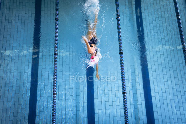 Vista ad alto angolo di una donna caucasica che indossa un costume da bagno e un berretto da bagno rosa che fa ictus freestyle in piscina — Foto stock
