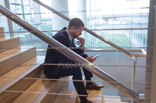 Vista lateral do empresário usando telefone celular em escadas em um prédio de escritórios moderno — Fotografia de Stock