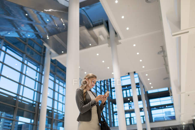 Низький кут зору бізнес-леді, використовуючи мобільний телефон у вестибюлі в сучасному офісі — стокове фото