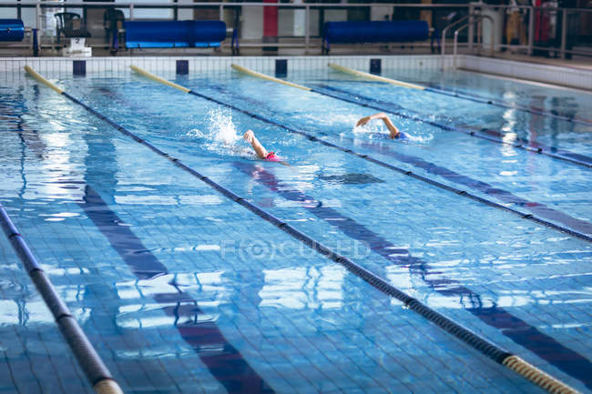 Side view of a young African-American and Caucasian women doing freestyle stroke in the pool — Stock Photo