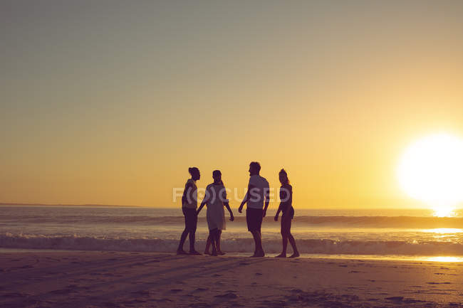 Вид ззаду групи різноманітних друзів, які розважаються на пляжі під час заходу сонця — стокове фото