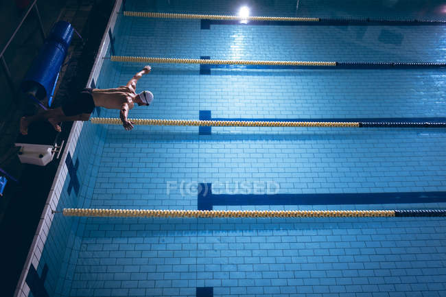 Hochwinkelaufnahme eines männlichen kaukasischen Schwimmers mit weißer Badekappe beim Tauchen im Schwimmbad — Stockfoto