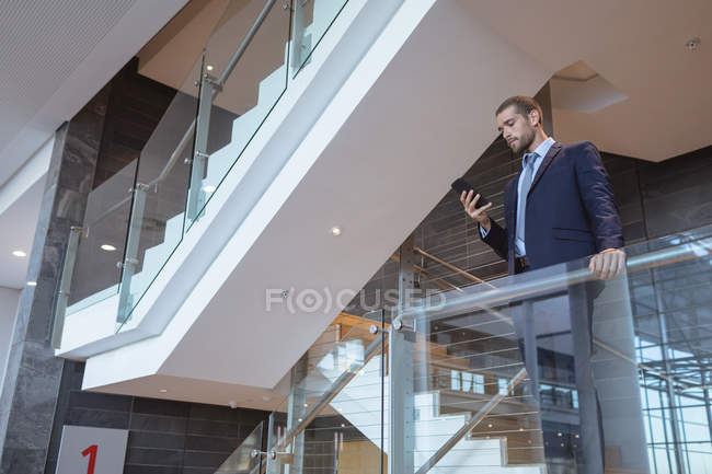 Vista a basso angolo dell'uomo d'affari che utilizza il telefono cellulare vicino alla ringhiera in un moderno edificio per uffici — Foto stock