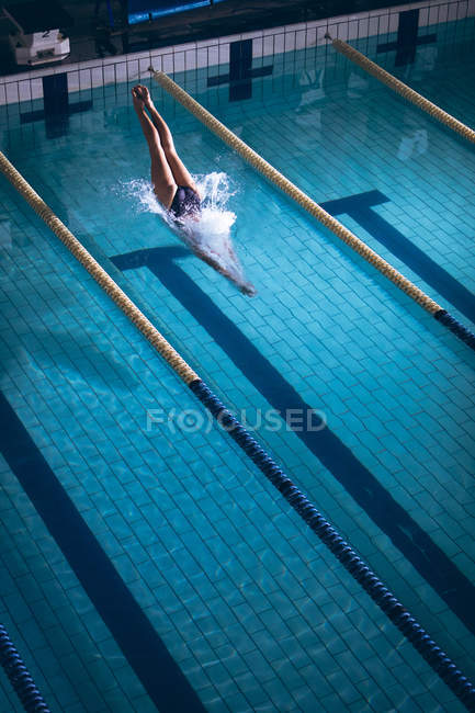 Высокий угол обзора белой женщины в купальнике и розовой плавательной шапке, ныряющей в бассейне — стоковое фото