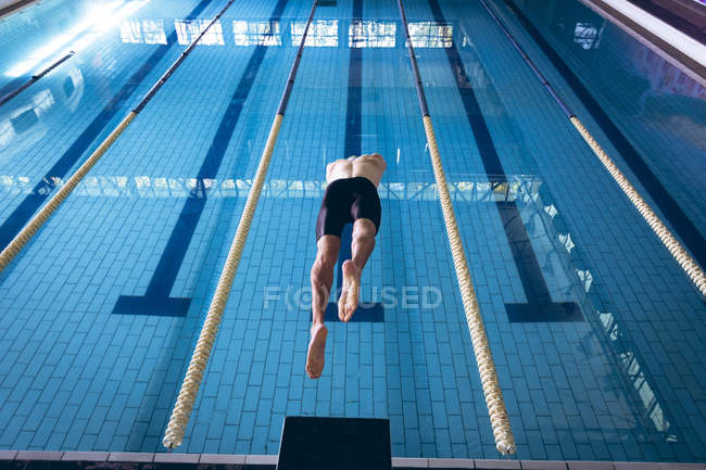 Rückansicht eines männlichen kaukasischen Schwimmers mit weißer Badekappe, der im Becken taucht — Stockfoto
