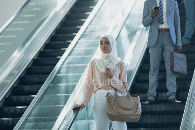 Front view of business woman in hijab using escalators in modern office — стоковое фото