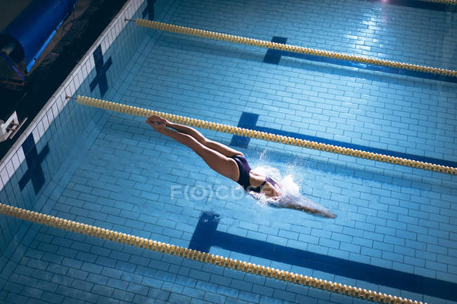 High angle view of a Caucasian woman wearing a swimsuit and a pink swimming cap diving in the swimming pool — Stock Photo