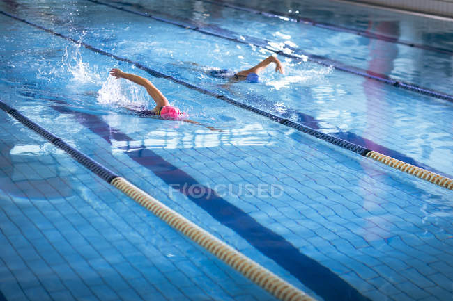 Вид сбоку на молодых афроамериканских и кавказских женщин, делающих фристайл в бассейне — стоковое фото
