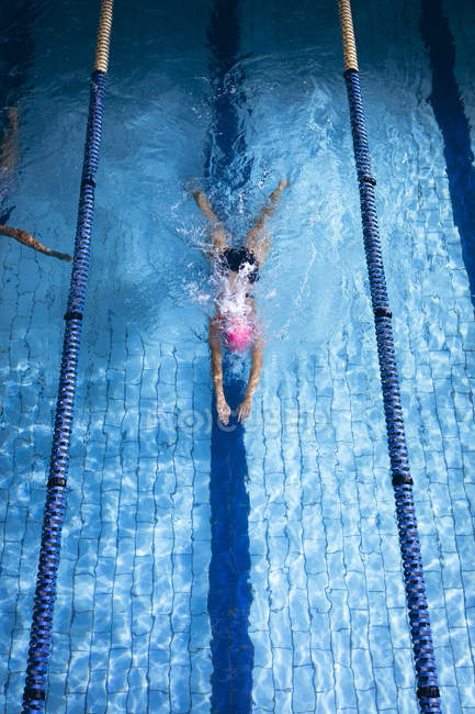 Vista ad alto angolo di una donna caucasica che indossa un berretto da bagno rosa e occhiali che fanno un colpo al seno in una piscina — Foto stock