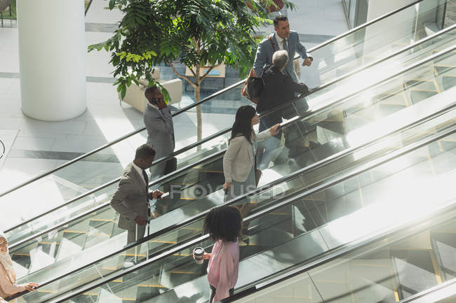 Vista aérea de diversos empresários usando escadas rolantes no escritório moderno — Fotografia de Stock