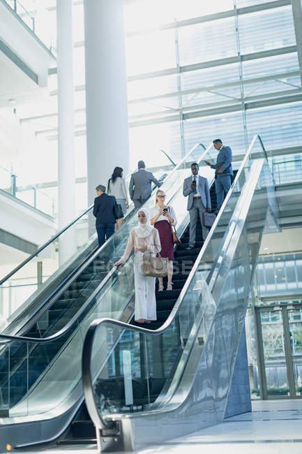 Vista lateral de diversas personas de negocios utilizando escaleras mecánicas en la oficina moderna - foto de stock