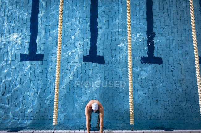 High angle view of male Caucasian swimmer wearing a white swimming cap and goggles holding on the side of the swimming pool — Stock Photo