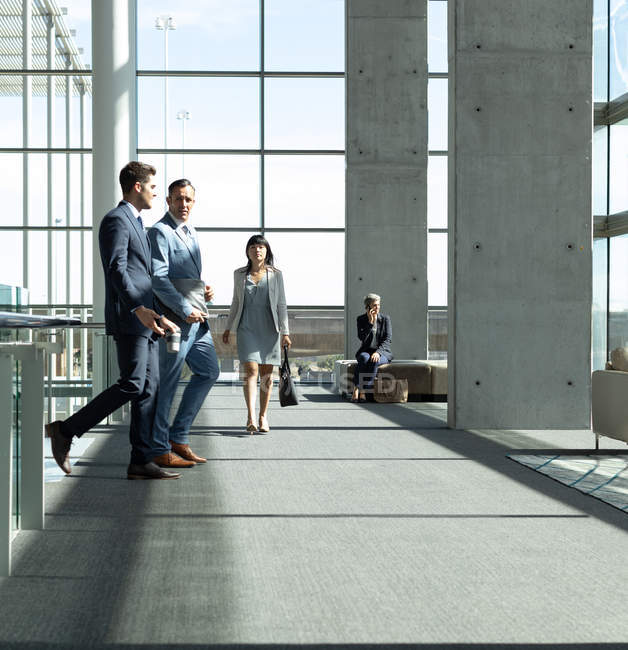 Vista lateral de los ejecutivos masculinos caucásicos interactuando entre sí mientras caminan en la oficina moderna - foto de stock