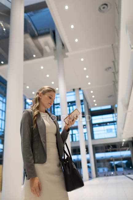 Vista de ángulo bajo de la mujer de negocios utilizando el teléfono móvil en el vestíbulo en la oficina moderna - foto de stock
