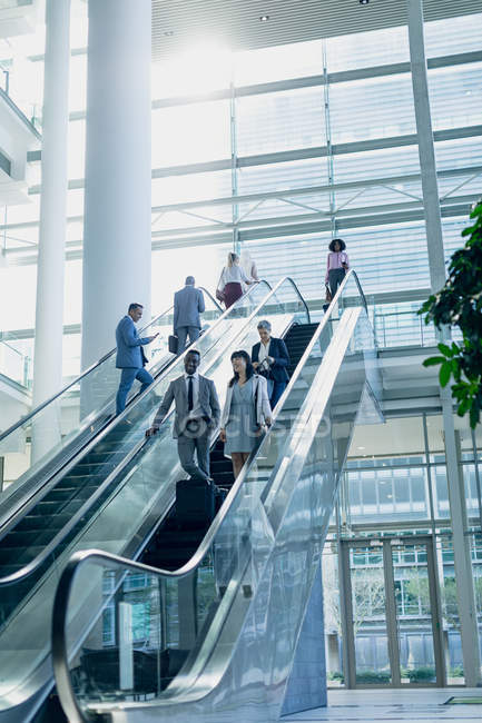Vue latérale de divers hommes d'affaires utilisant des escaliers roulants dans un bureau moderne — Photo de stock