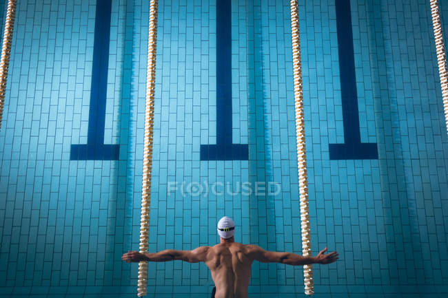 High angle view of a male Caucasian swimmer wearing a white swimming cap diving in the swimming pool — Stock Photo