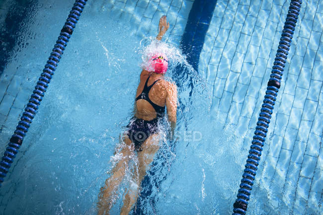 High angle view of a Caucasian woman wearing a pink swimming cap and goggles doing a freestyle stroke in a swimming pool — Stock Photo