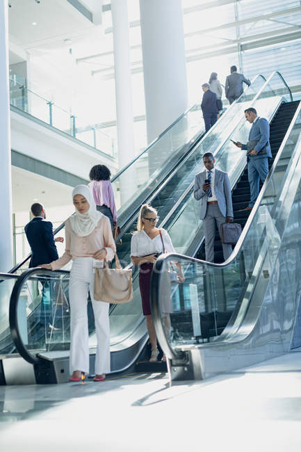 Vista lateral de diversas personas de negocios utilizando escaleras mecánicas en la oficina moderna - foto de stock