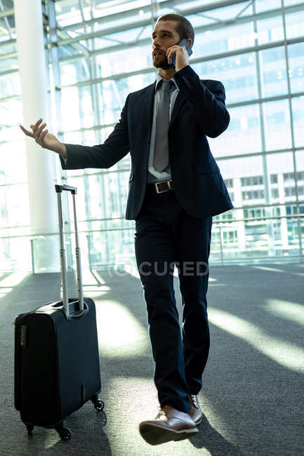 Вид спереду бізнесмена з сумкою для візків, що розмовляє на мобільному телефоні в сучасному офісному будинку — стокове фото