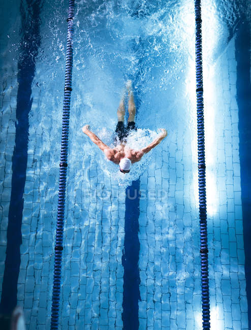 Hochwinkelaufnahme eines männlichen kaukasischen Schwimmers mit weißer Badekappe bei einem Schmetterlingsschlag im Schwimmbad — Stockfoto