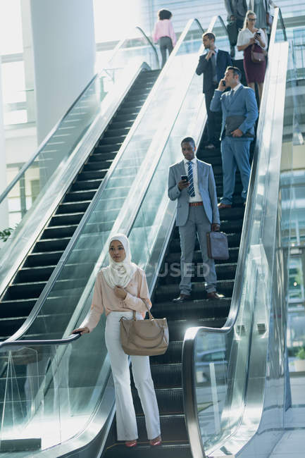 Вид спереду на різних бізнесменів, що використовують ескалатори в сучасному офісі — стокове фото