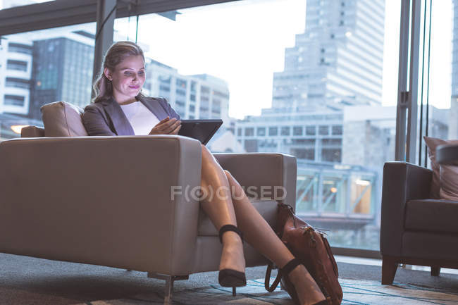 Vista frontal de la mujer de negocios que trabaja en la tableta digital en el sofá en el vestíbulo en la oficina moderna - foto de stock