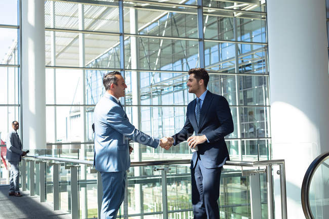 Side view of Caucasian male executives shaking hands while standing in modern office — Stock Photo