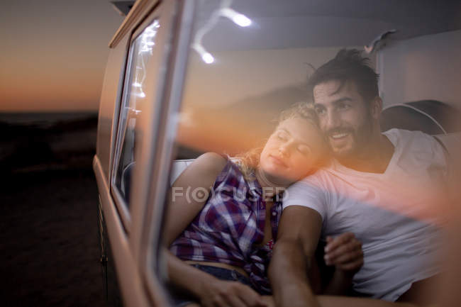 Вид спереди романтической кавказской пары, сидящей вместе в фургоне на пляже на закате — стоковое фото