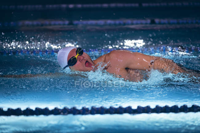 Vista laterale di un nuotatore caucasico maschio con cuffia e occhiali bianchi che fa un ictus freestyle in piscina — Foto stock