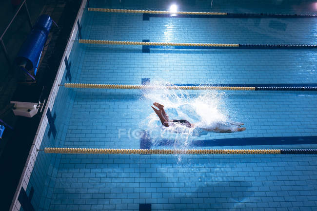 Vista de alto ângulo de um nadador caucasiano masculino que usa um gorro branco mergulhando na piscina — Fotografia de Stock