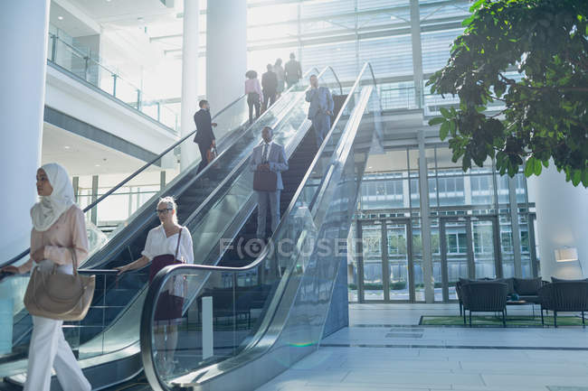 Вид сбоку на разнообразных бизнесменов, использующих эскалаторы в современном офисе — стоковое фото