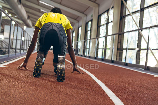 Vue arrière d'un athlète afro-américain handicapé en position de départ sur piste de course dans un centre de remise en forme — Photo de stock